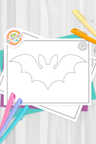 Black and white bat outline template printable on top of blue-green and purple sheets with assorted markers on a dark grey background. printed pdf version from Kids activities blog.